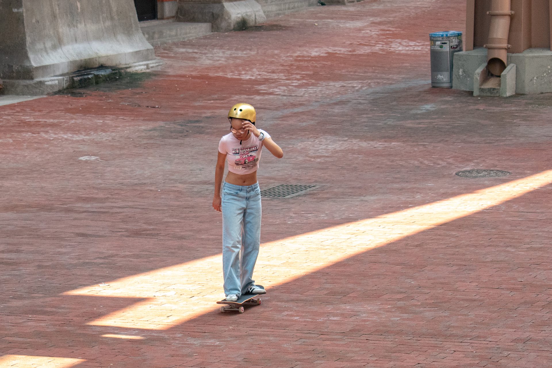 A single young person on a skateboard crossing a wide empty brick plaza, long shadow, nobody else in frame.