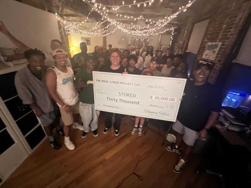 Hunter Hess holding a thirty thousand dollar check made out to STOKED, surrounded by coaches, mentors and alumni at the STOKED office in Brooklyn.